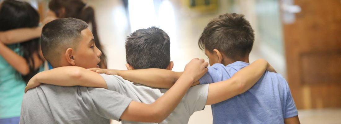 Three students walking in the hallway with arms around each other